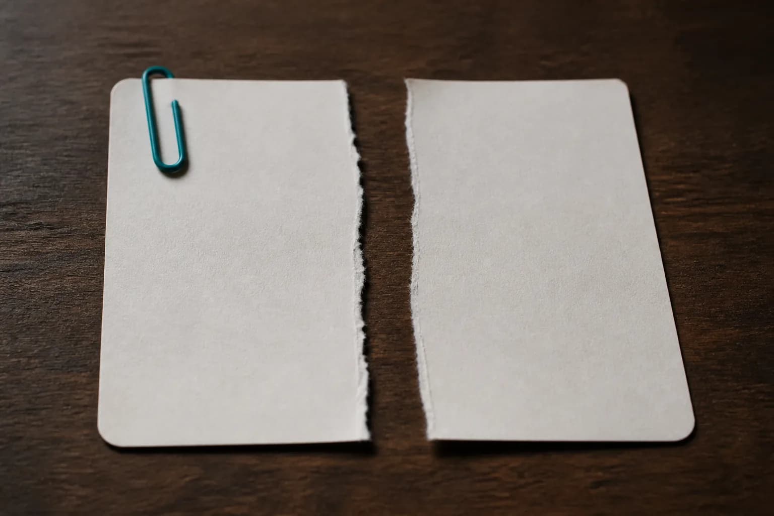 A blank paper receipt torn cleanly into two equal halves, with a small teal paperclip on one half